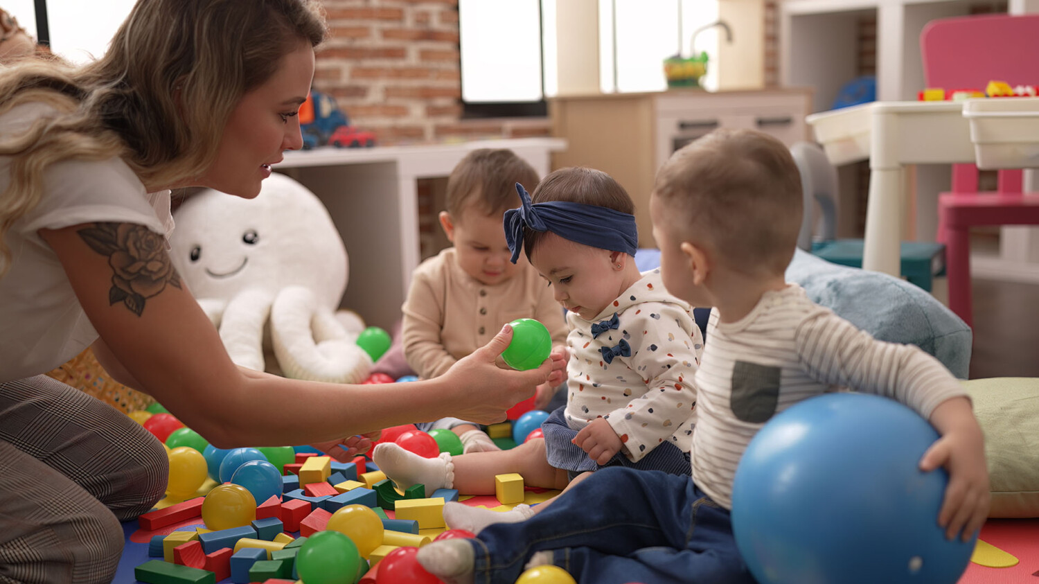 Teacher and preschool students playing with balls sitting on floor at kindergarten